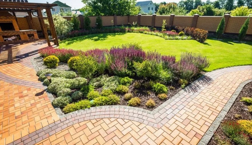 Intricate brick patio design with a curved flower bed and stone wall.