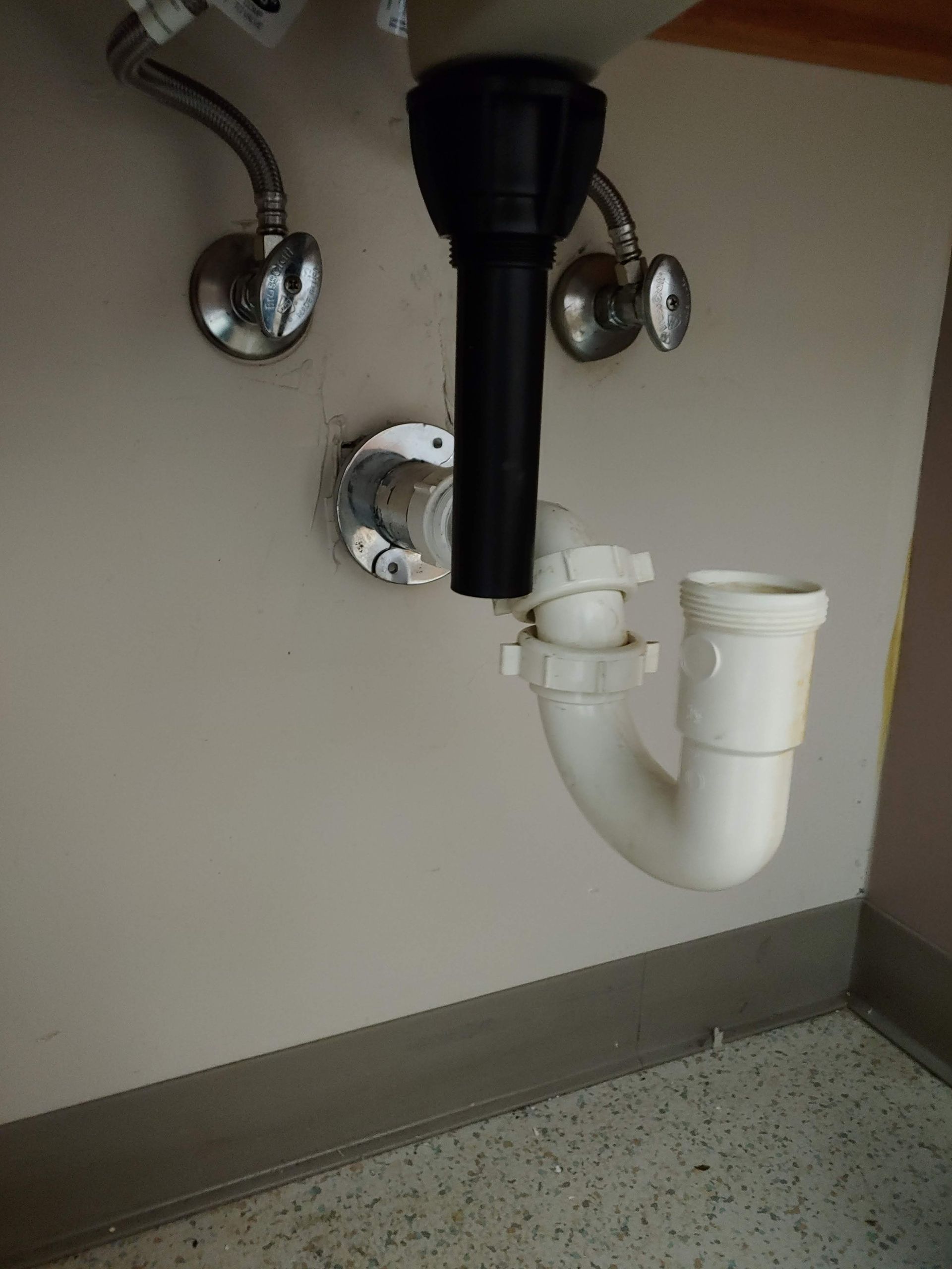 A sink with a black pipe and a white pipe underneath it.