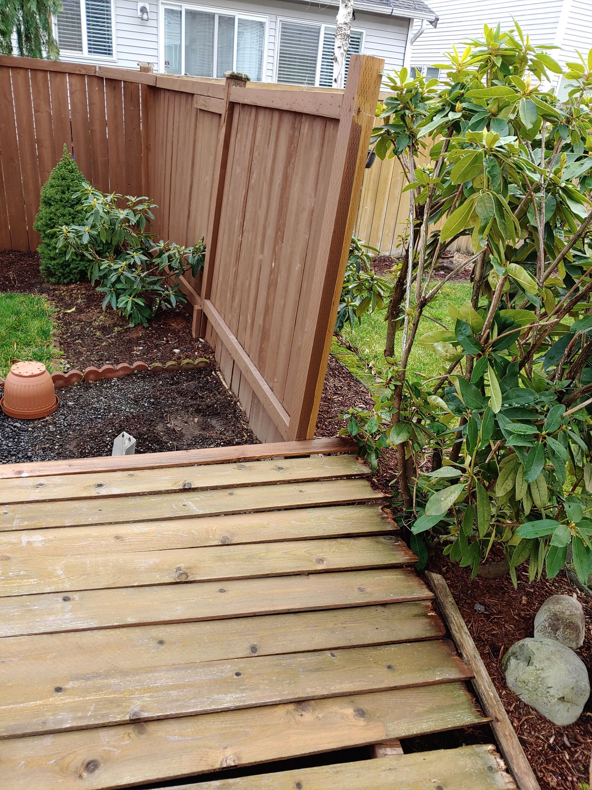 A wooden walkway leading to a wooden fence in a backyard.