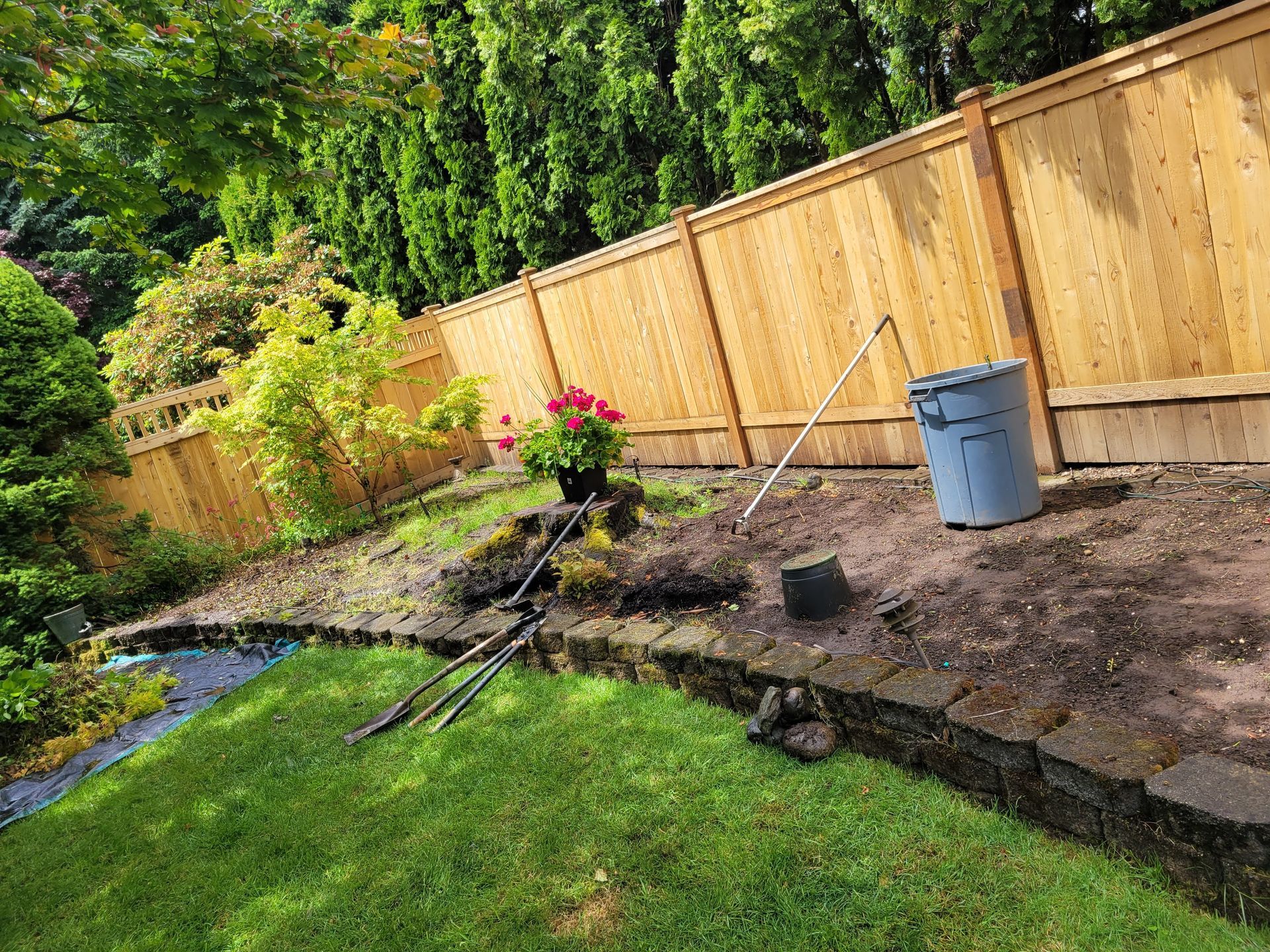 A wooden fence is surrounding a garden with a bucket and shovel.
