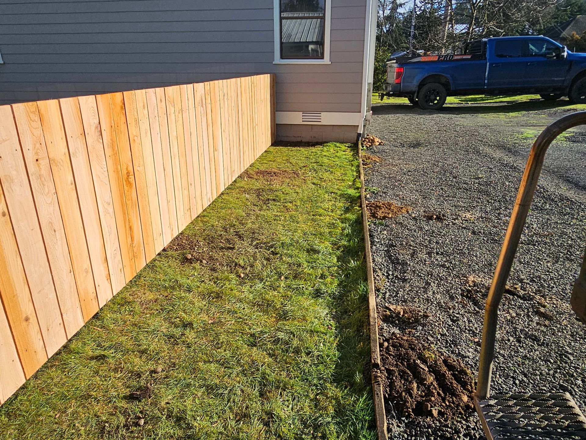 A blue truck is parked in front of a house next to a wooden fence.