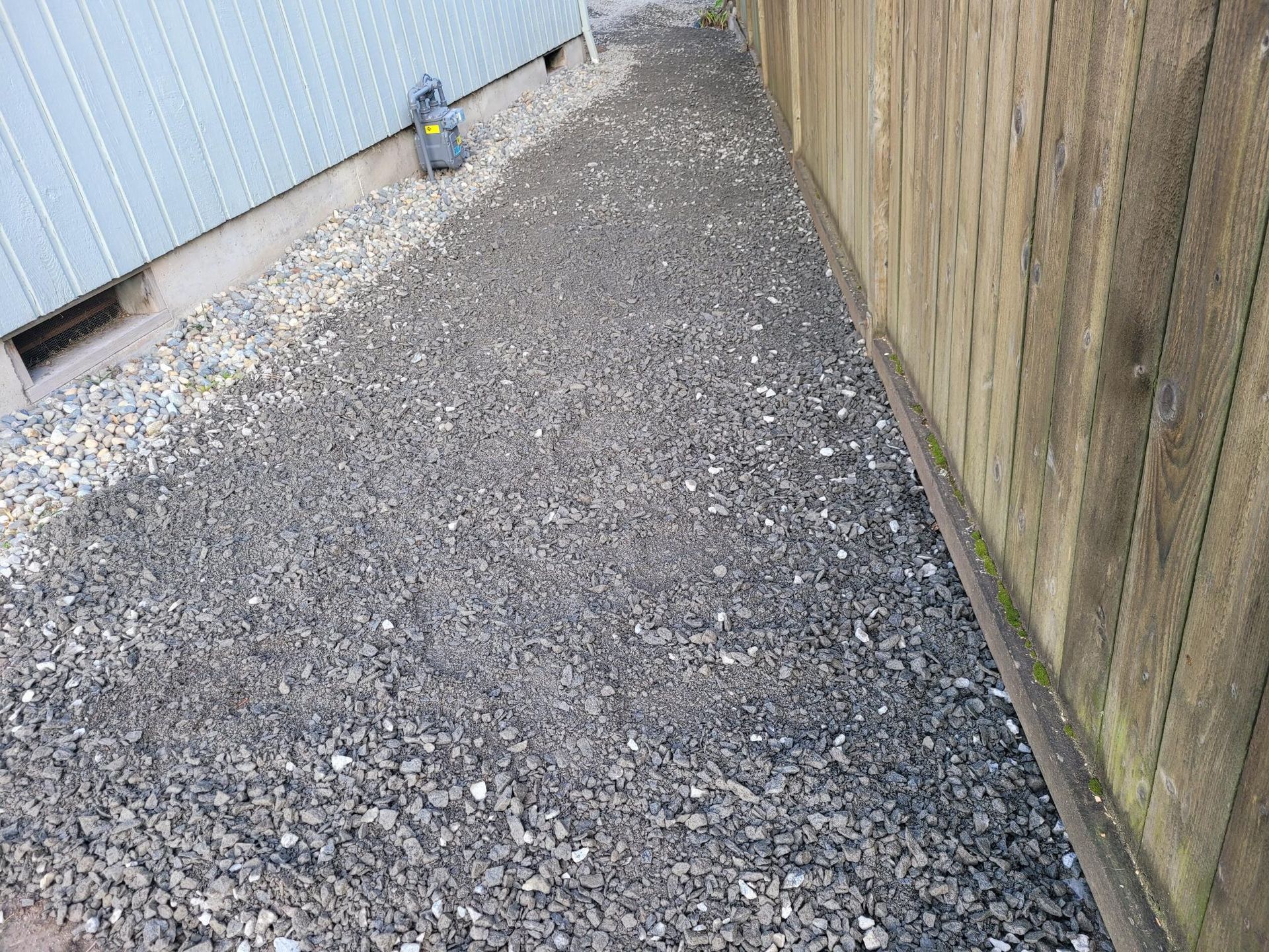 A gravel path leading to a wooden fence next to a building.