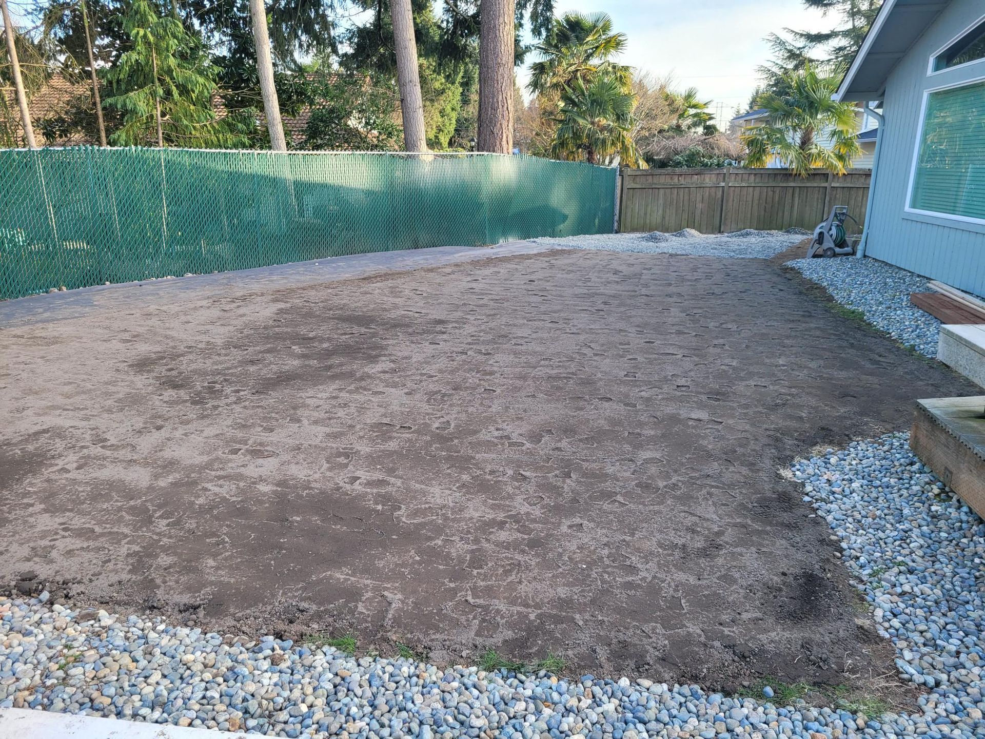 A backyard with gravel and dirt in front of a house.