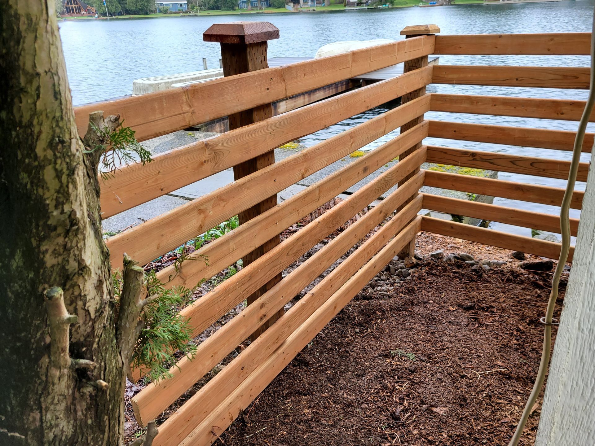 A wooden fence with a tree in the foreground and a lake in the background.