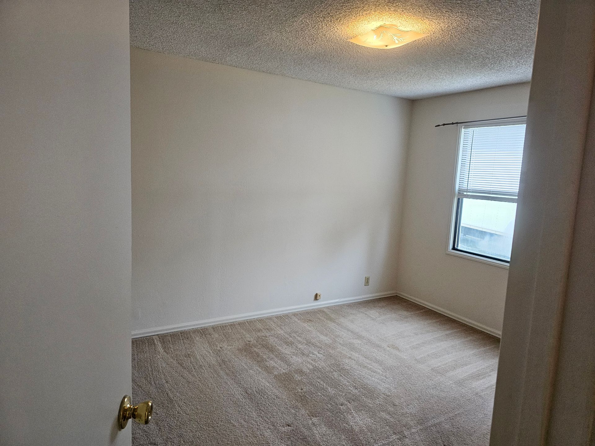 An empty bedroom with a carpeted floor and a window.