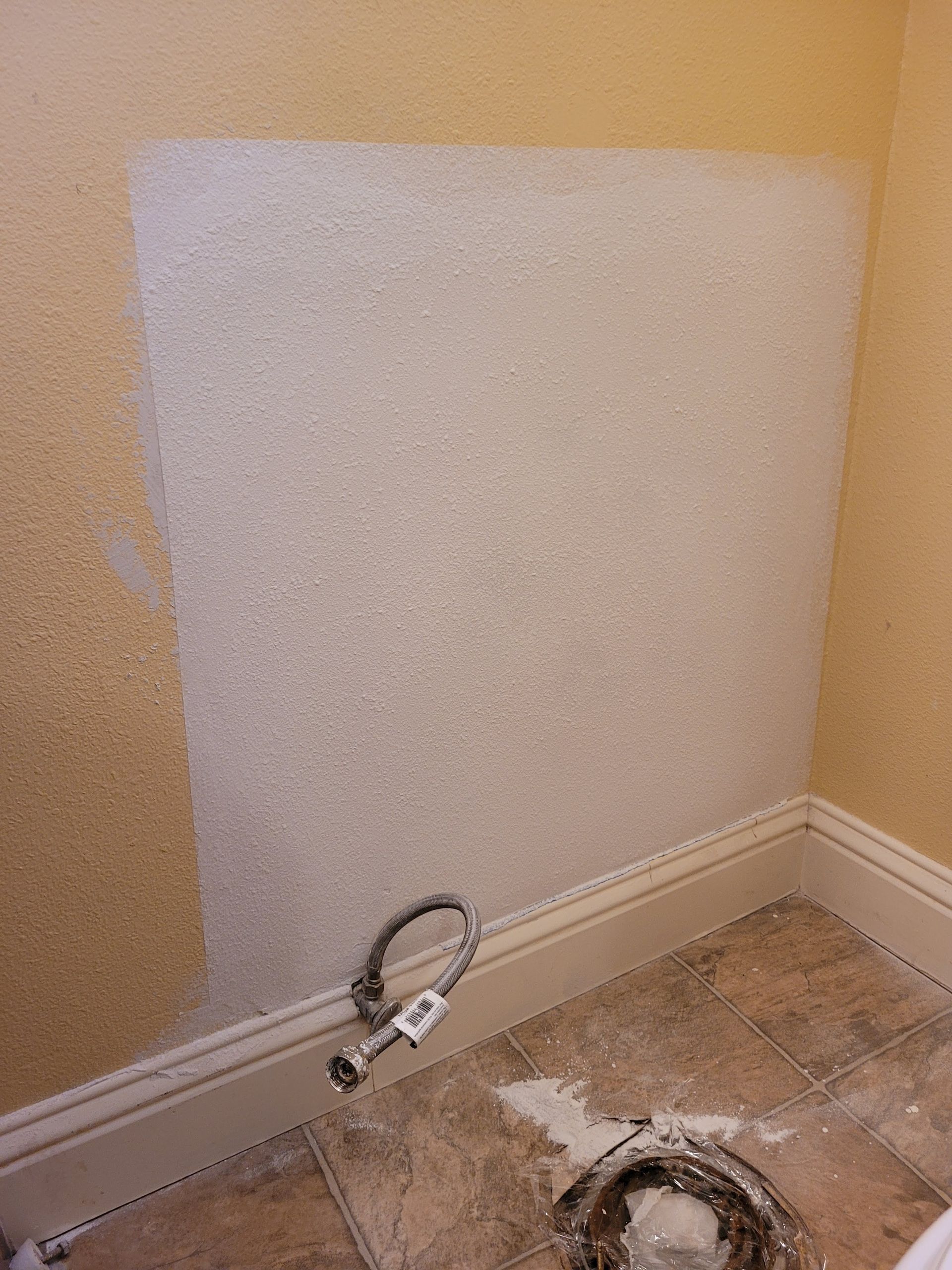 A bathroom with a white wall and a faucet on the floor.