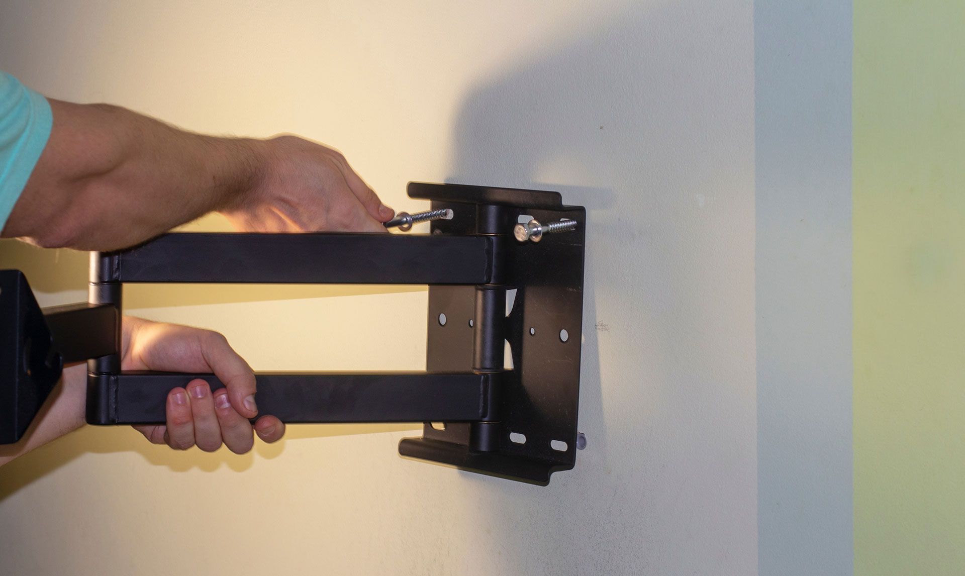 A person attaches a black, articulated wall-mount TV bracket to a wall.