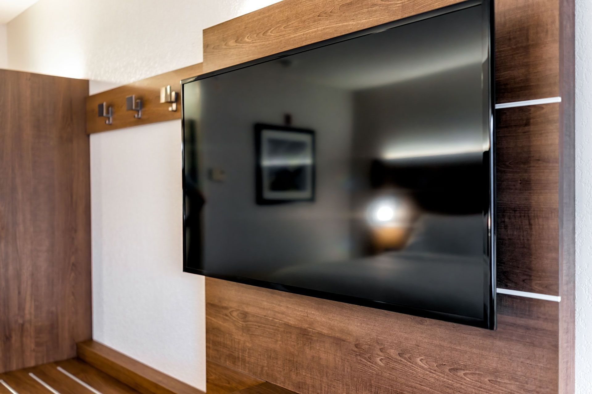 A large flat-screen television mounted on a wood-paneled wall, reflecting a blurred hotel bedroom.