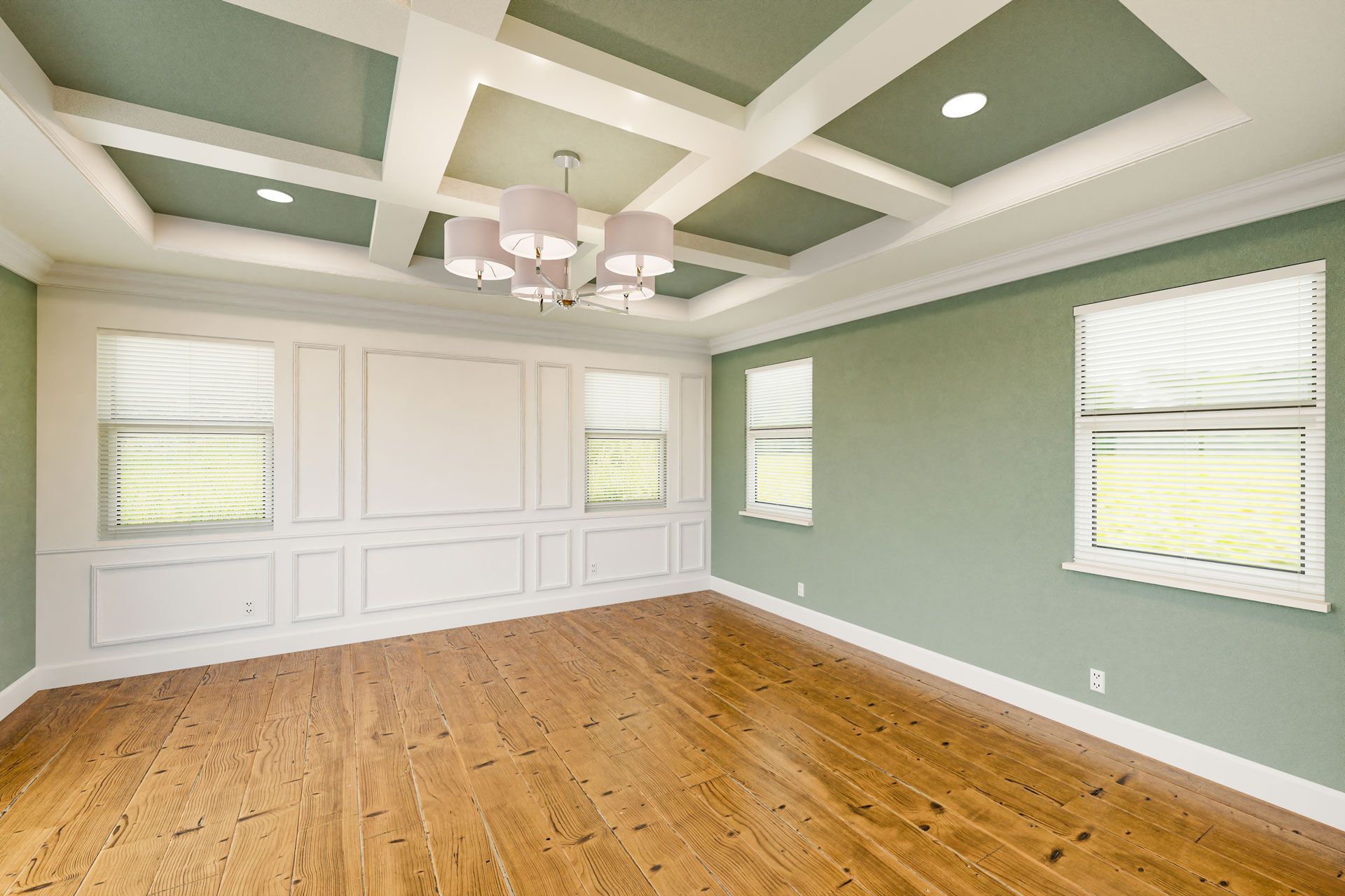 A bright, empty room with sage green walls, white wainscoting, light wood floors, and a coffered ceiling with a chandelier.