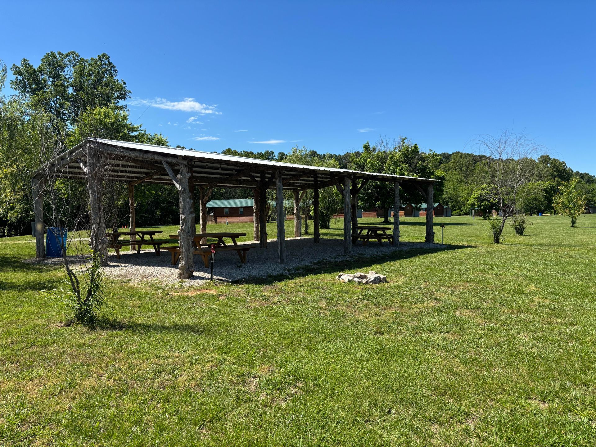 A group of people are sitting under a picnic shelter in a park.