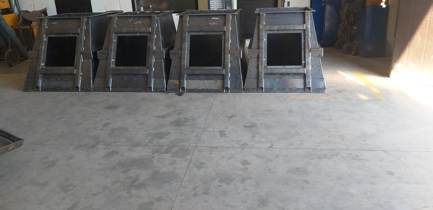 Quattro scivoli metallici industriali sono disposti in fila sul pavimento di cemento di un'officina.