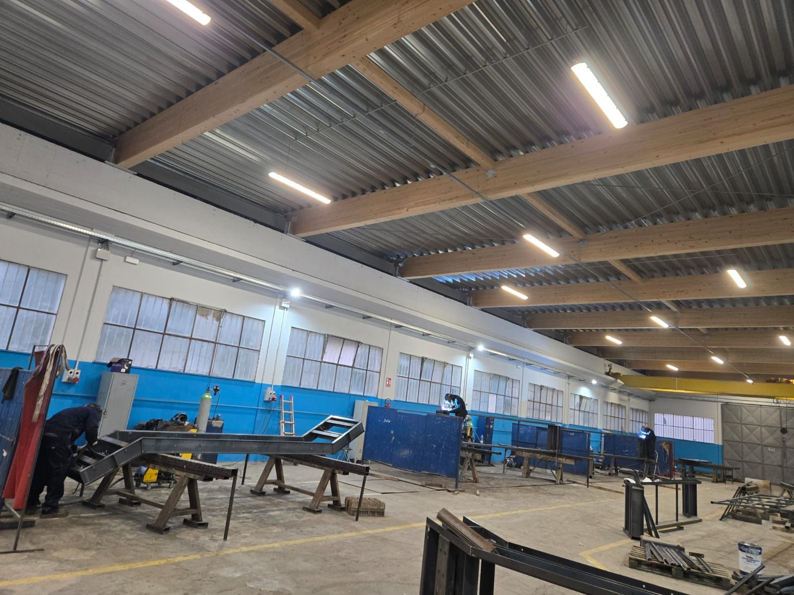 Ampia veduta di una spaziosa officina industriale con strutture metalliche, utensili e operai sotto soffitti alti.