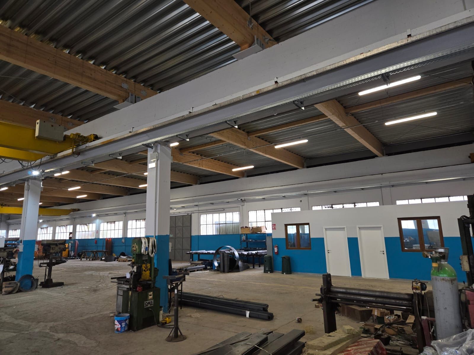Un'ampia officina industriale con soffitti alti, grandi pilastri bianchi e pareti dipinte di blu.