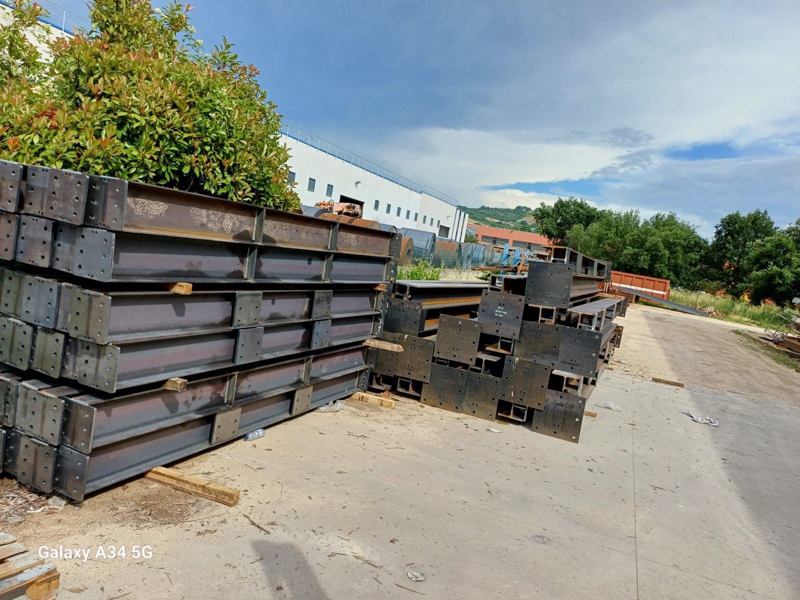 Pile di travi d'acciaio industriali stoccate all'aperto in un cortile in una giornata nuvolosa.
