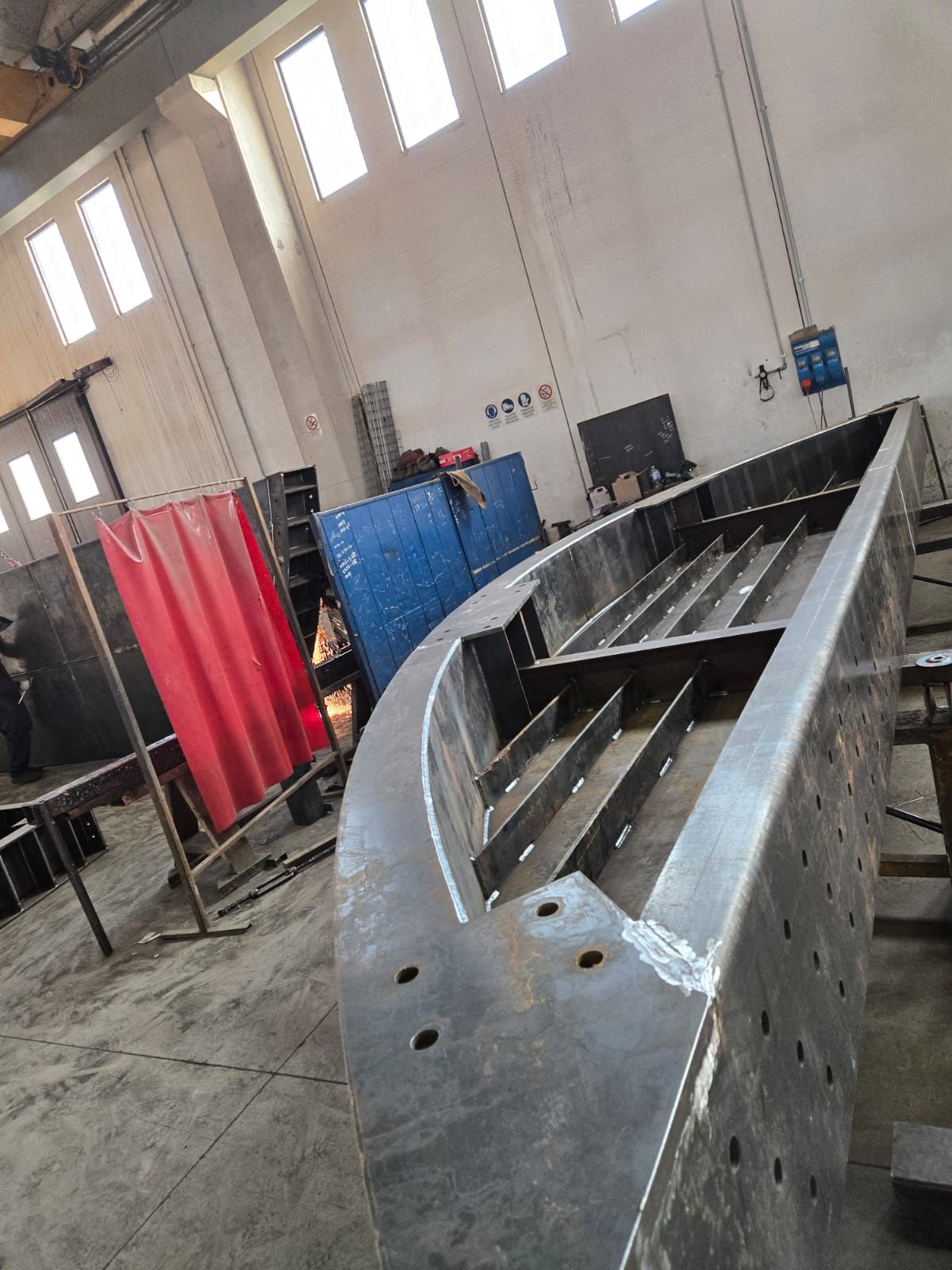 Un'officina metallurgica che mostra al centro della stanza la struttura di una barca in costruzione, con costole e travi in ​​acciaio.