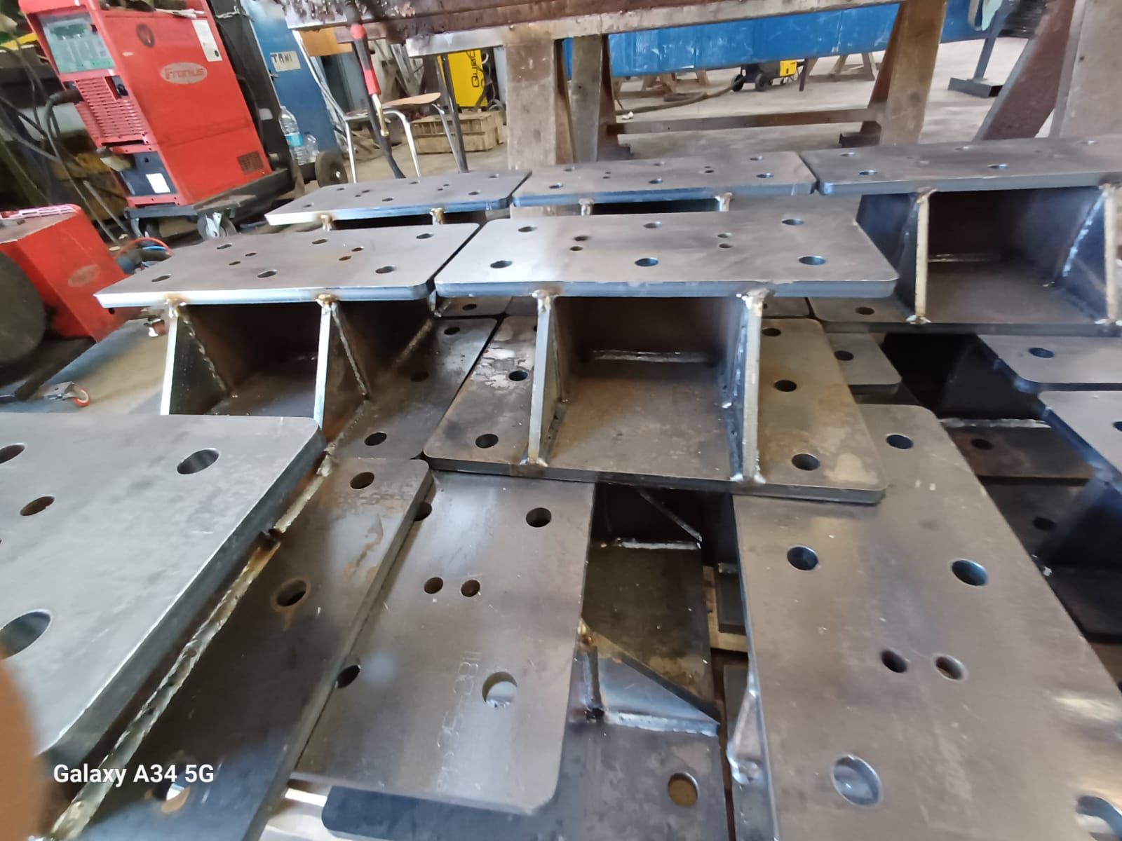 Diverse piastre di montaggio industriali in acciaio a sezione a I, impilate e dotate di fori preforati per i bulloni, in un ambiente di officina.