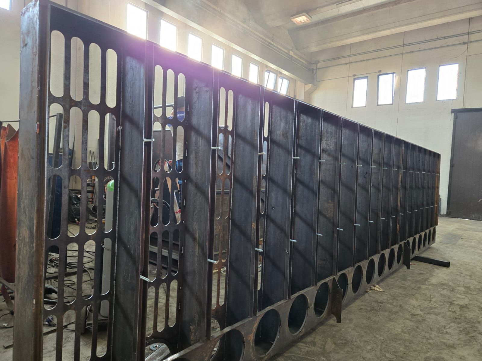Una grande struttura in acciaio prefabbricata con pannelli verticali perforati, situata in un'officina industriale.