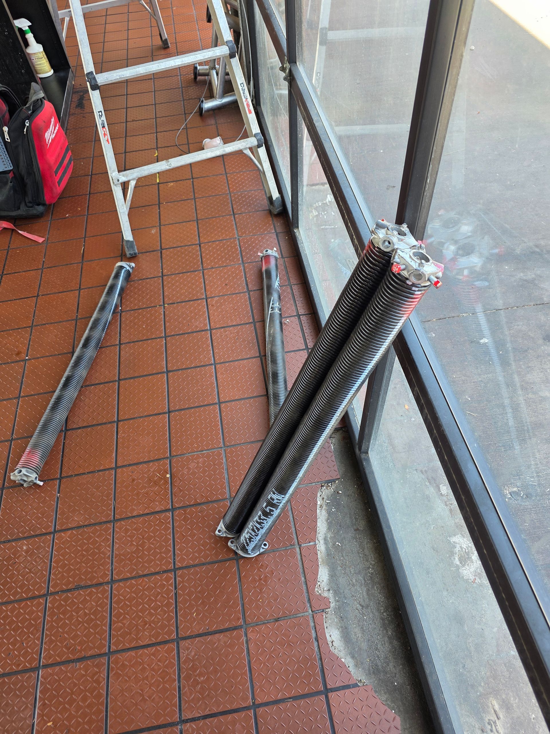 Black garage door springs on a tile floor near a window and a ladder.
