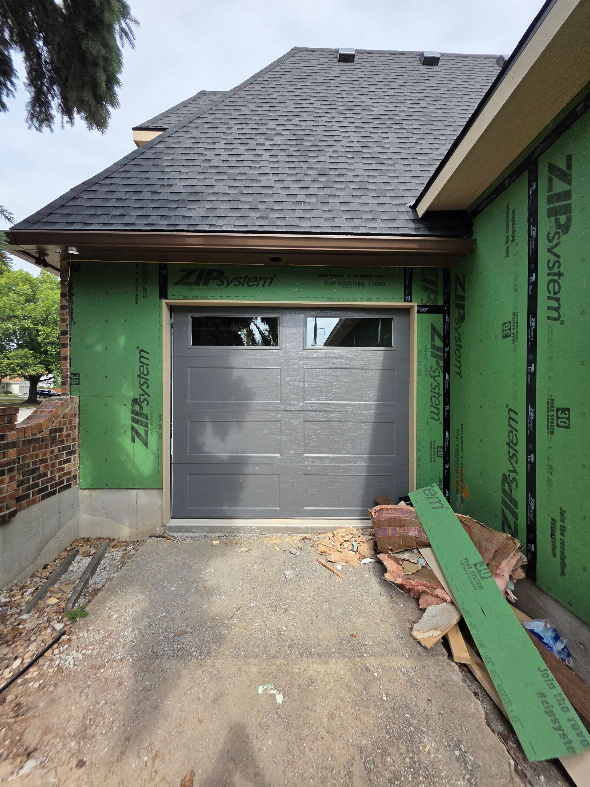 Gray garage door in a house under construction. Exterior walls are green, gravel driveway.