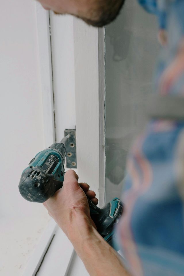 Person using a drill to install a door hinge on a white door frame.