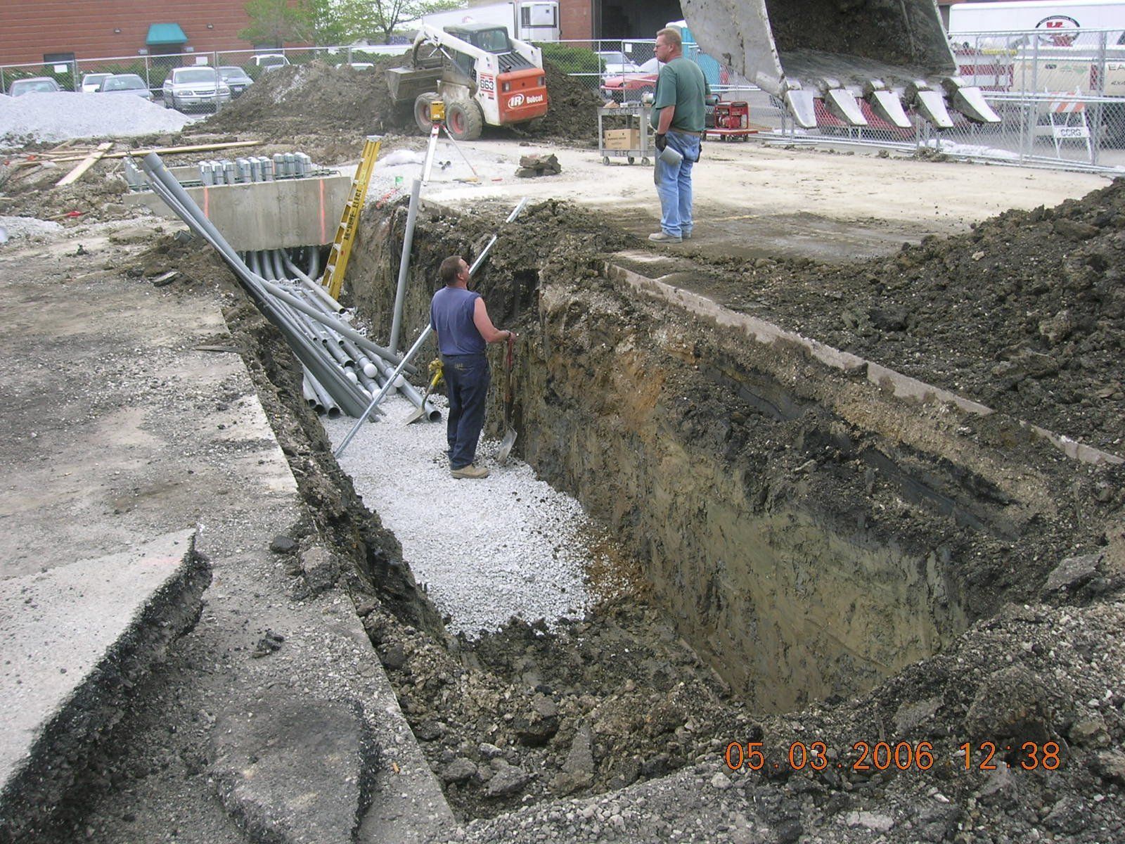 A man is digging a hole in the ground with a bulldozer in the background