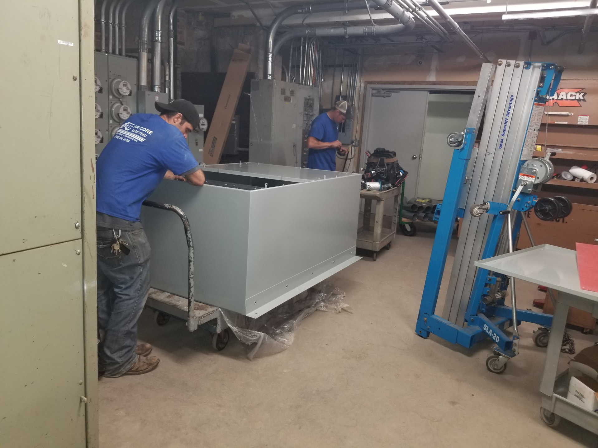 A man in a blue shirt is pushing a large metal box on a cart.