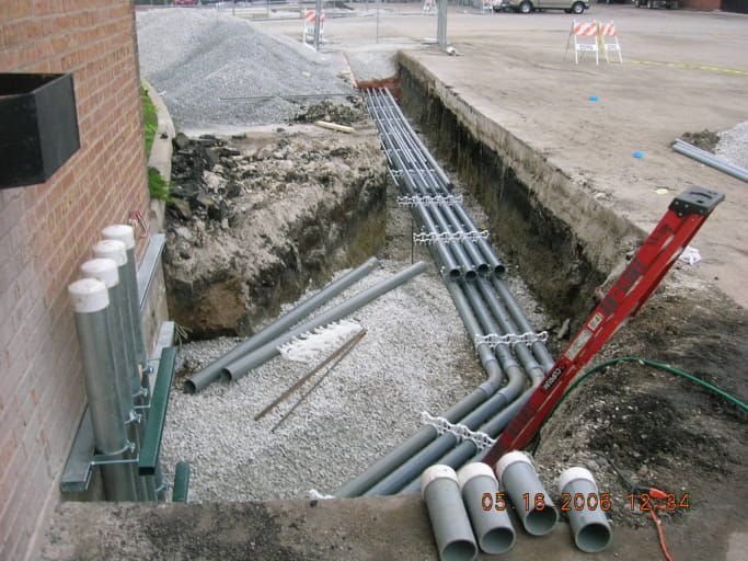 A bunch of pipes are laying on the ground in a trench