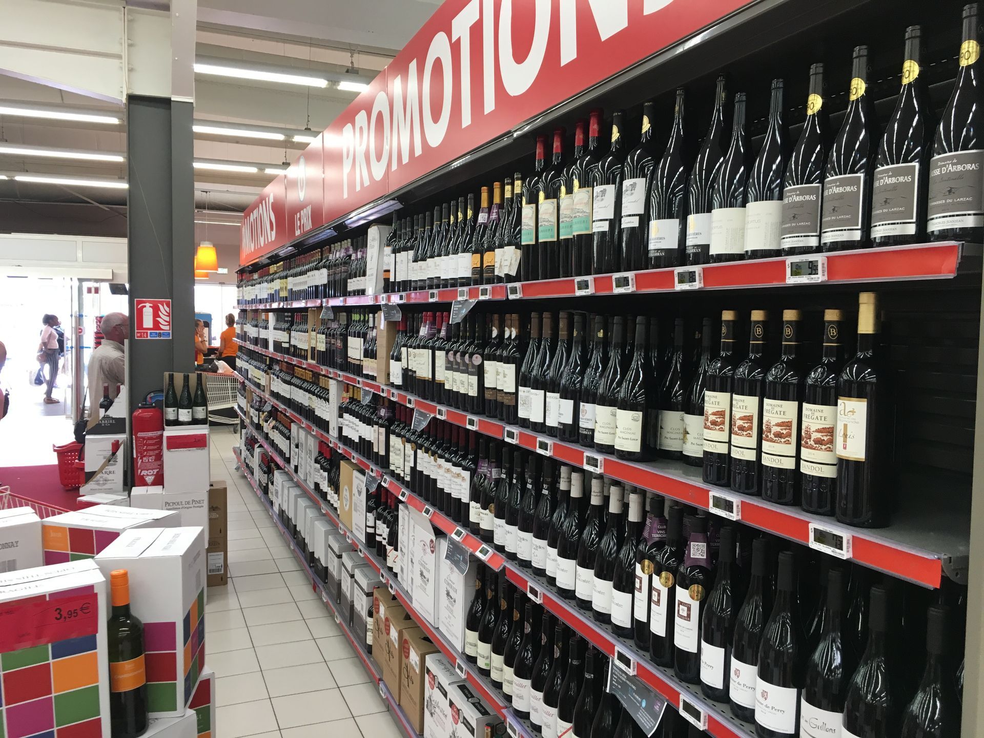 Rows of wine bottles on shelves in a supermarket, under a 