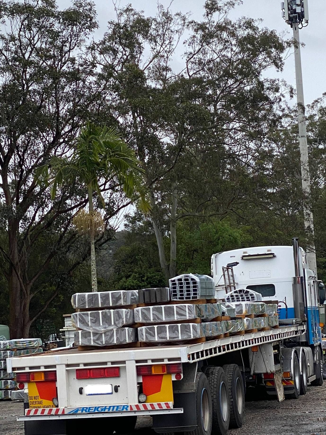 Truck With a Flatbed Trailer Loaded With Wrapped Metal Beams — Concrete Sleepers NSW in Central Coast, NSW