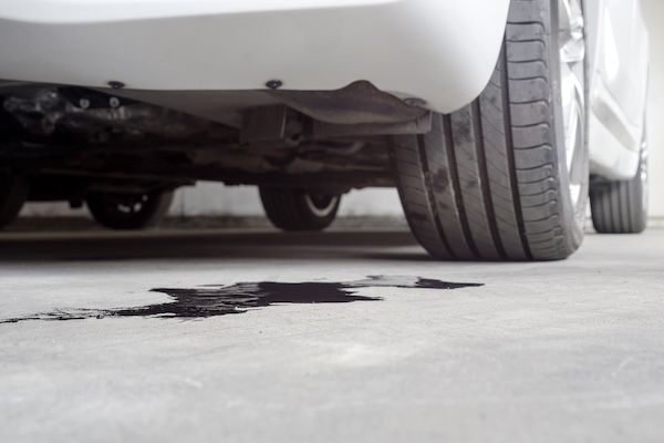 Black oil puddle on concrete floor under the rear of a white car 