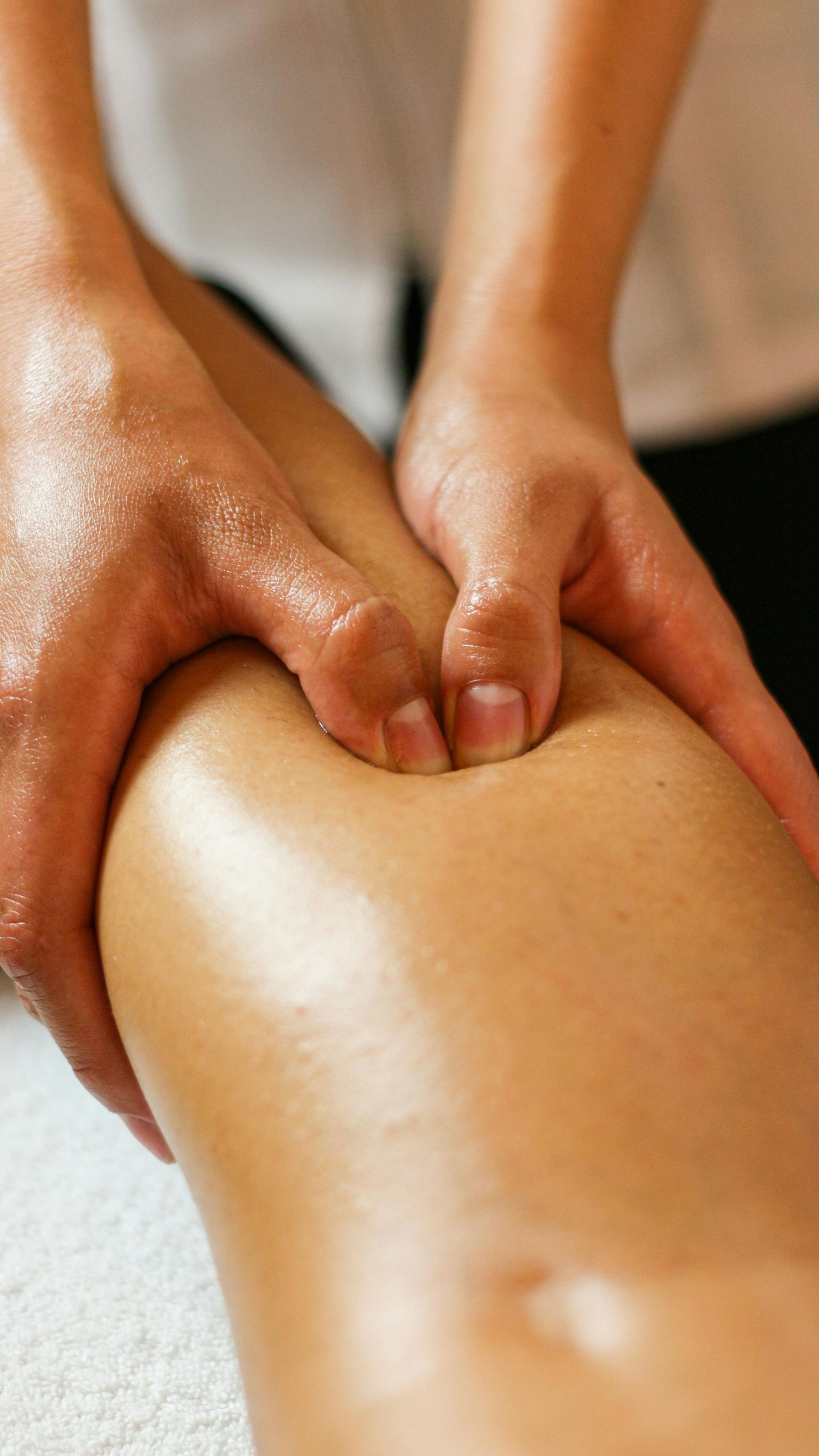 Hands massaging a leg, applying pressure. Skin is tanned, glossy.