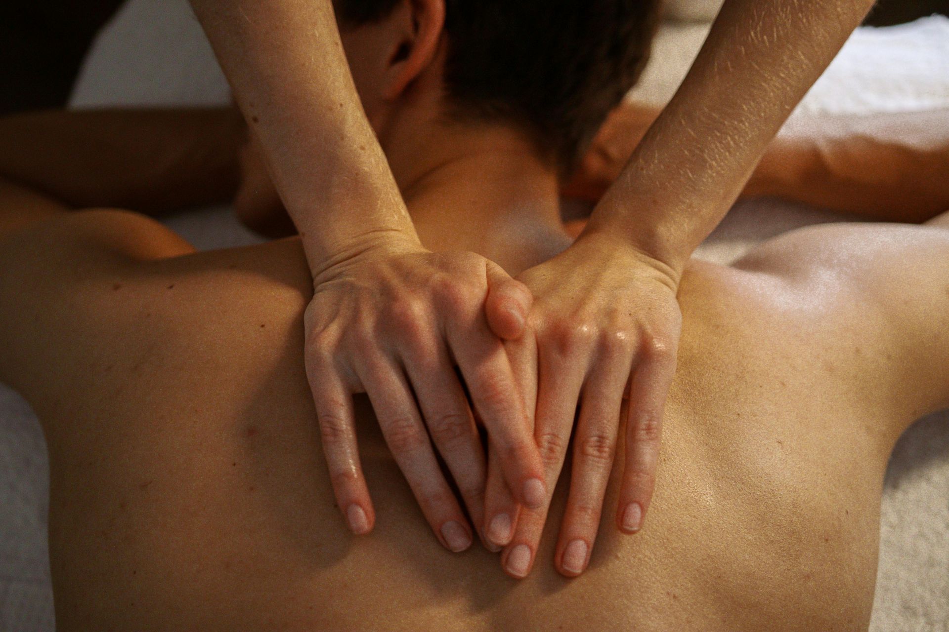 Hands massaging the back of a person lying face down on a white surface.