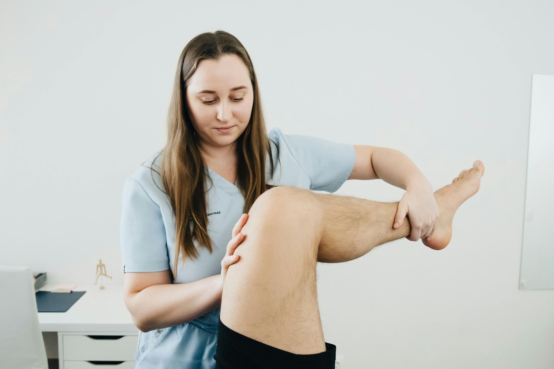 Female therapist examining a patient's leg, likely assessing knee flexibility in a clinic setting.