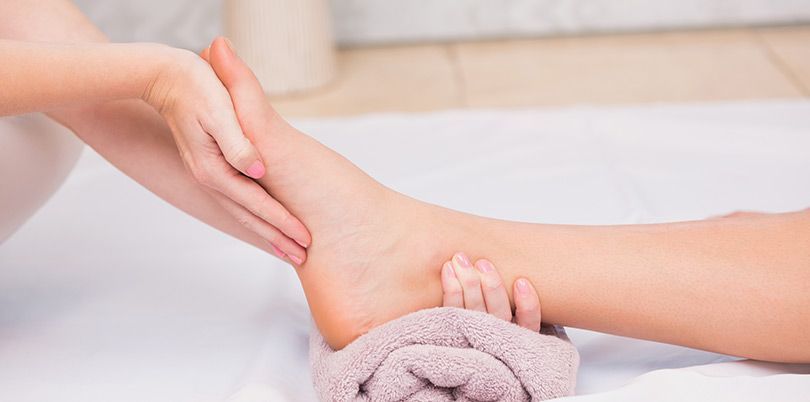 Person receiving a foot massage. Hands massaging the foot and ankle on a towel, indoor setting.