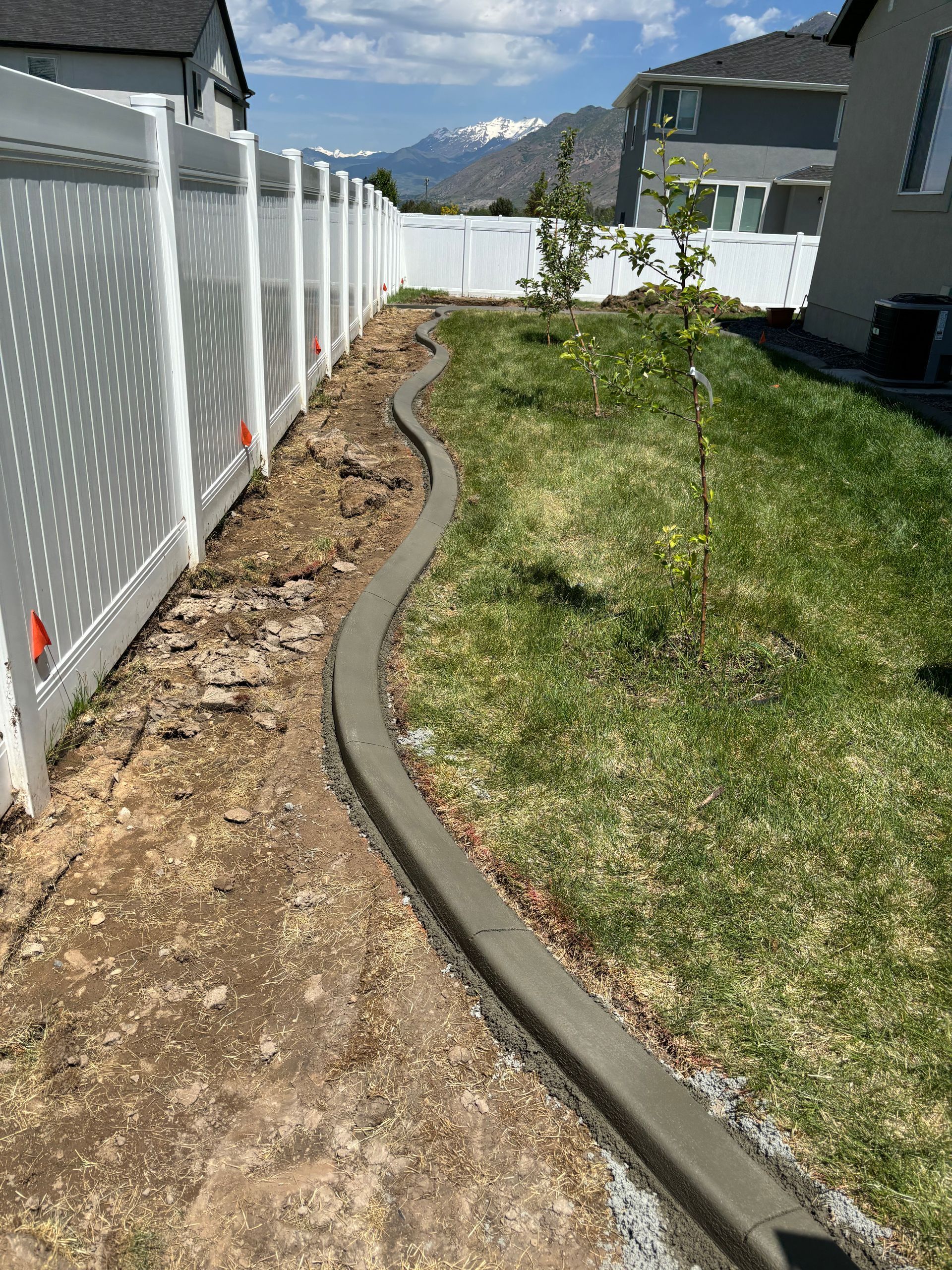 Judd Landscape & Curbing LLC | a concrete curb is being installed in a backyard next to a white fence.