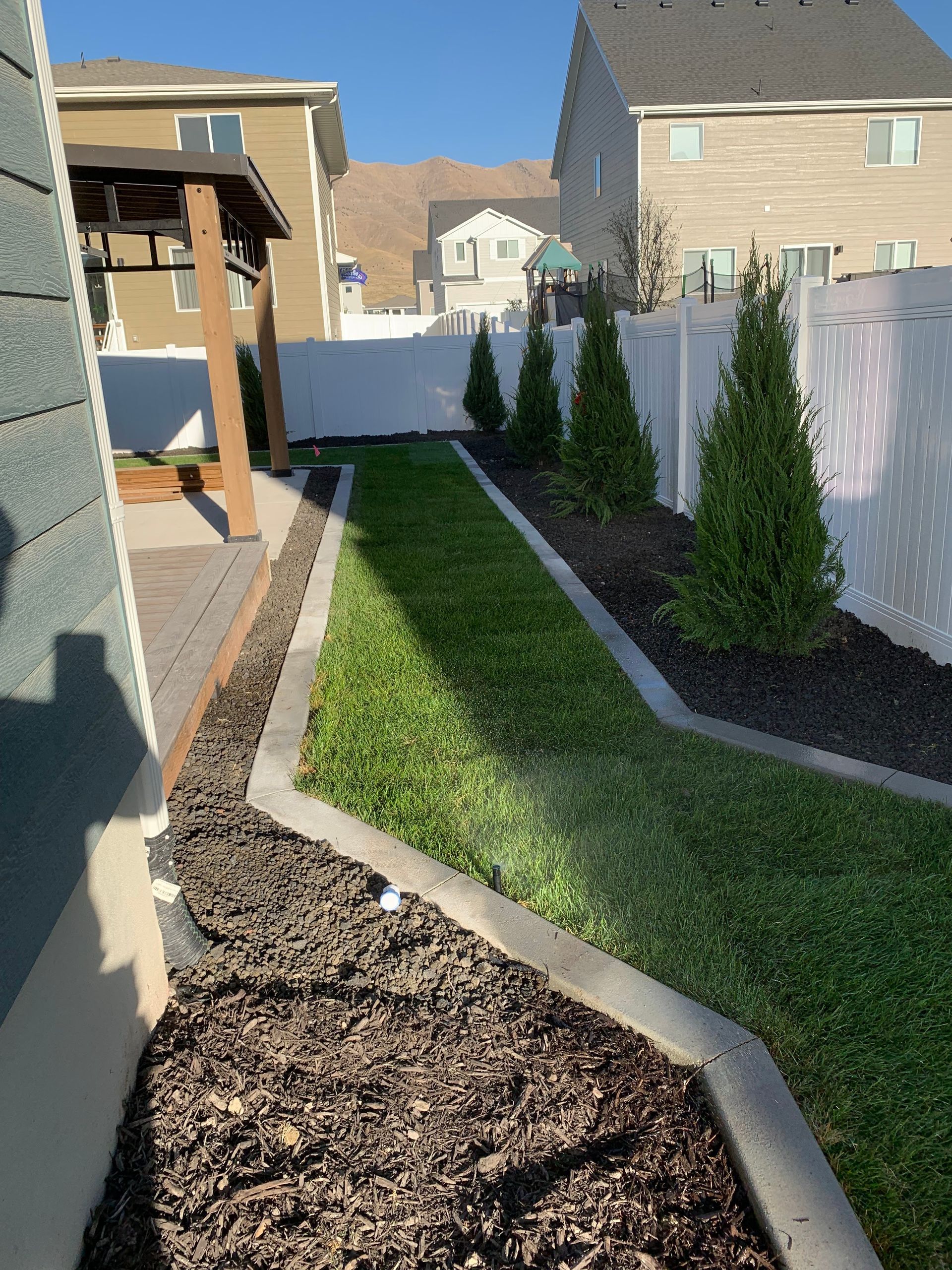 Judd Landscape & Curbing LLC | a backyard with a white fence and a lush green lawn