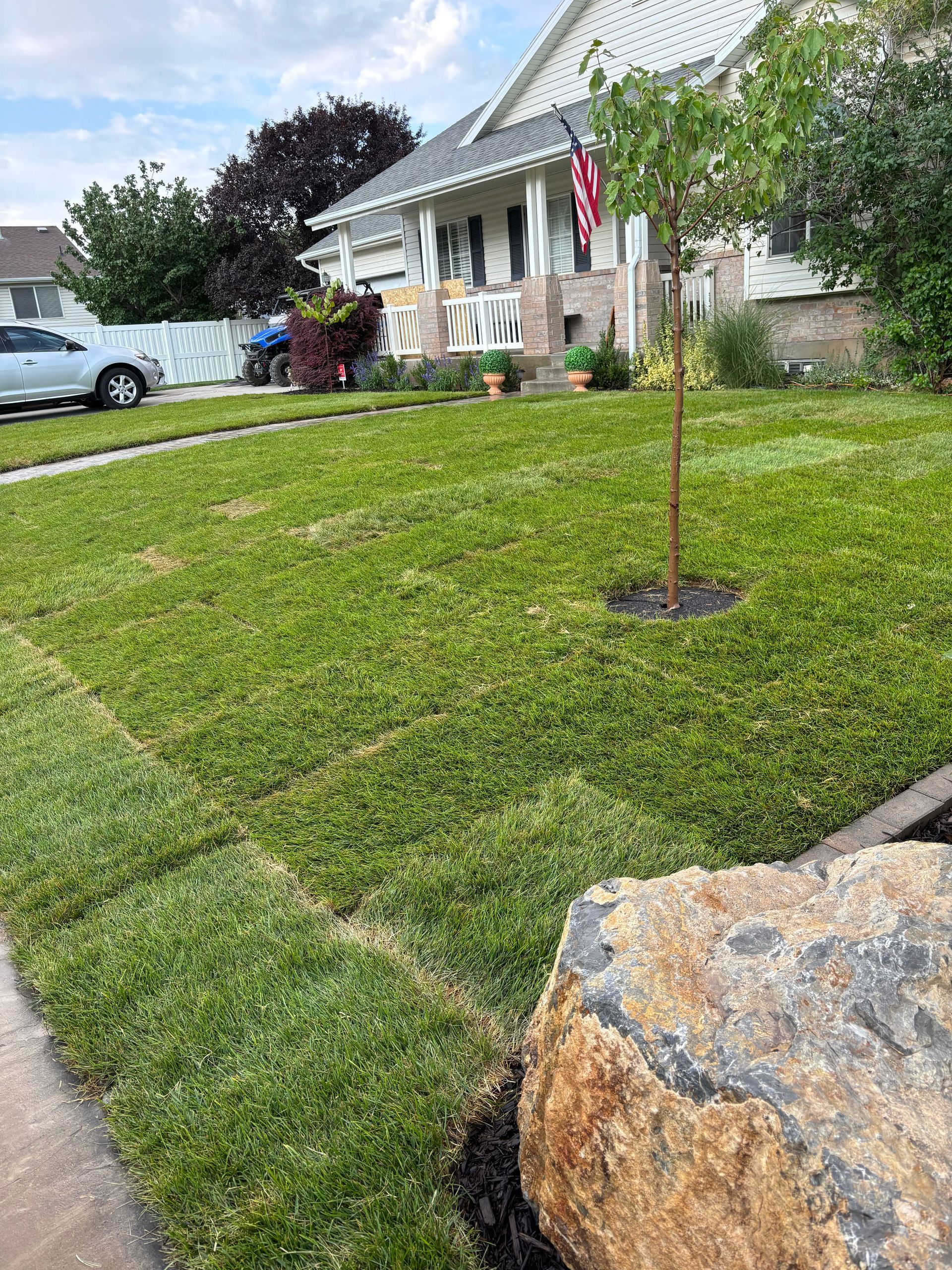 Judd Landscape & Curbing LLC | a lush green lawn with a tree in the middle of it in front of a house.