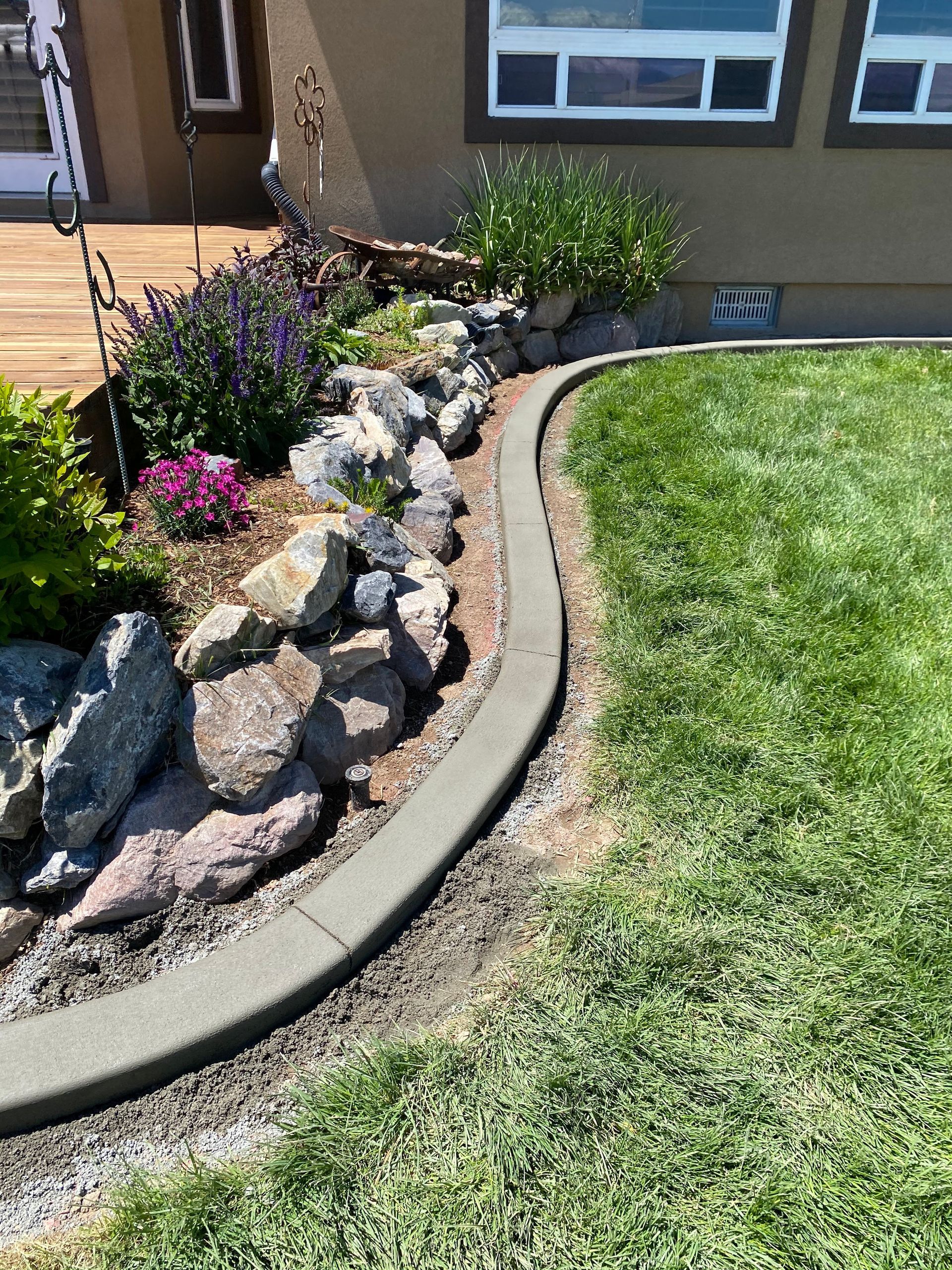 Judd Landscape & Curbing LLC | a concrete curb surrounds a rock garden in front of a house.