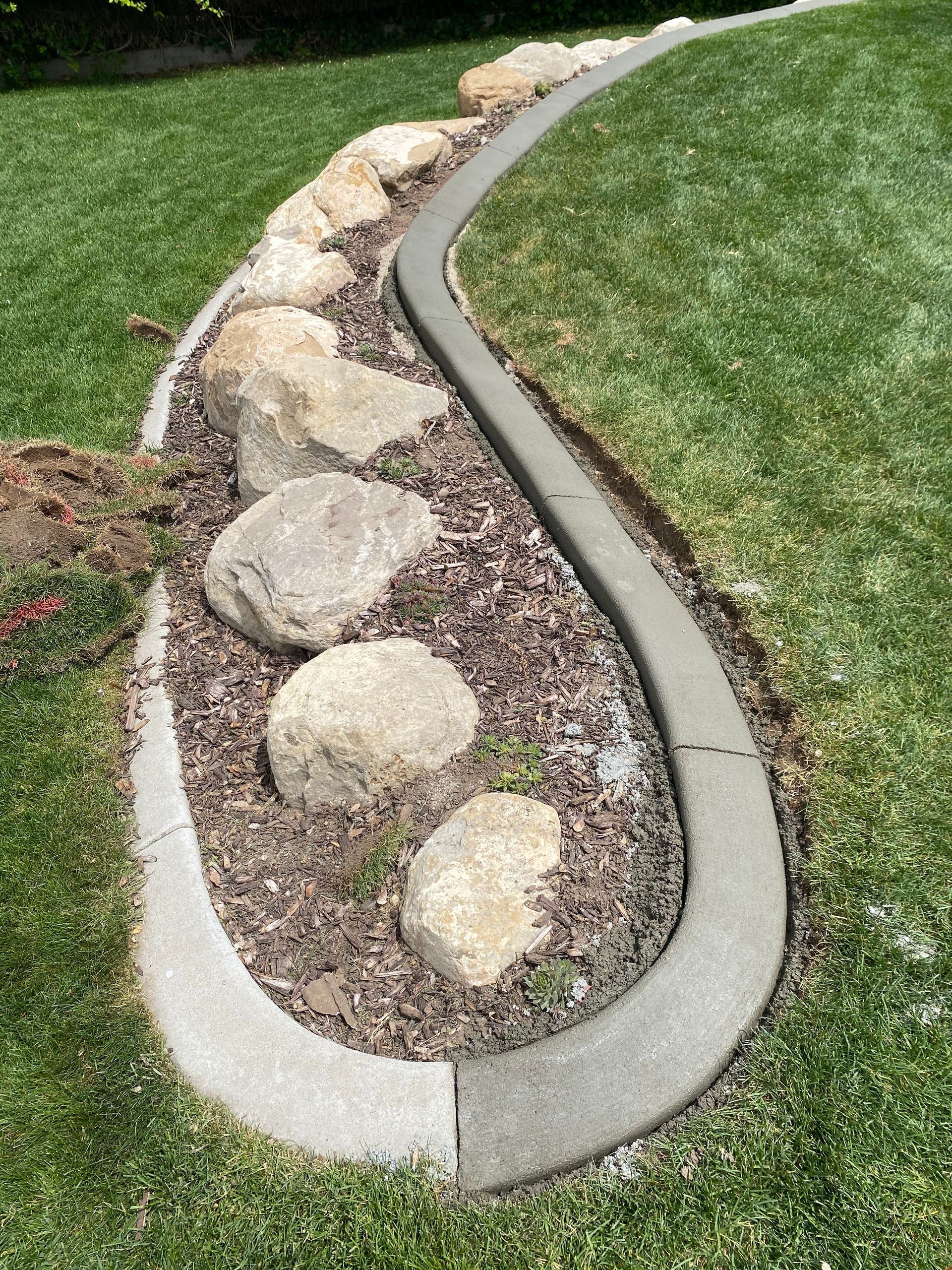 Judd Landscape & Curbing LLC | a concrete curb is surrounded by rocks in a lush green yard.