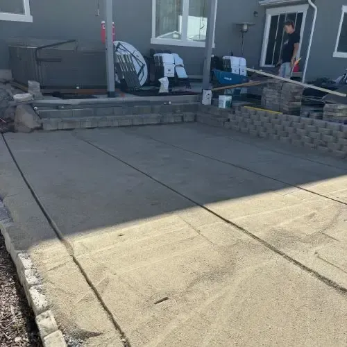 Judd Landscape & Curbing LLC | a man is standing on a concrete patio in front of a house.