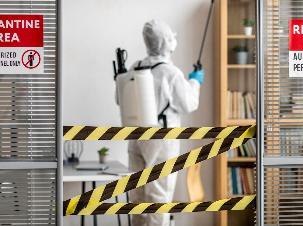 A man in a protective suit is spraying a room with a sprayer.