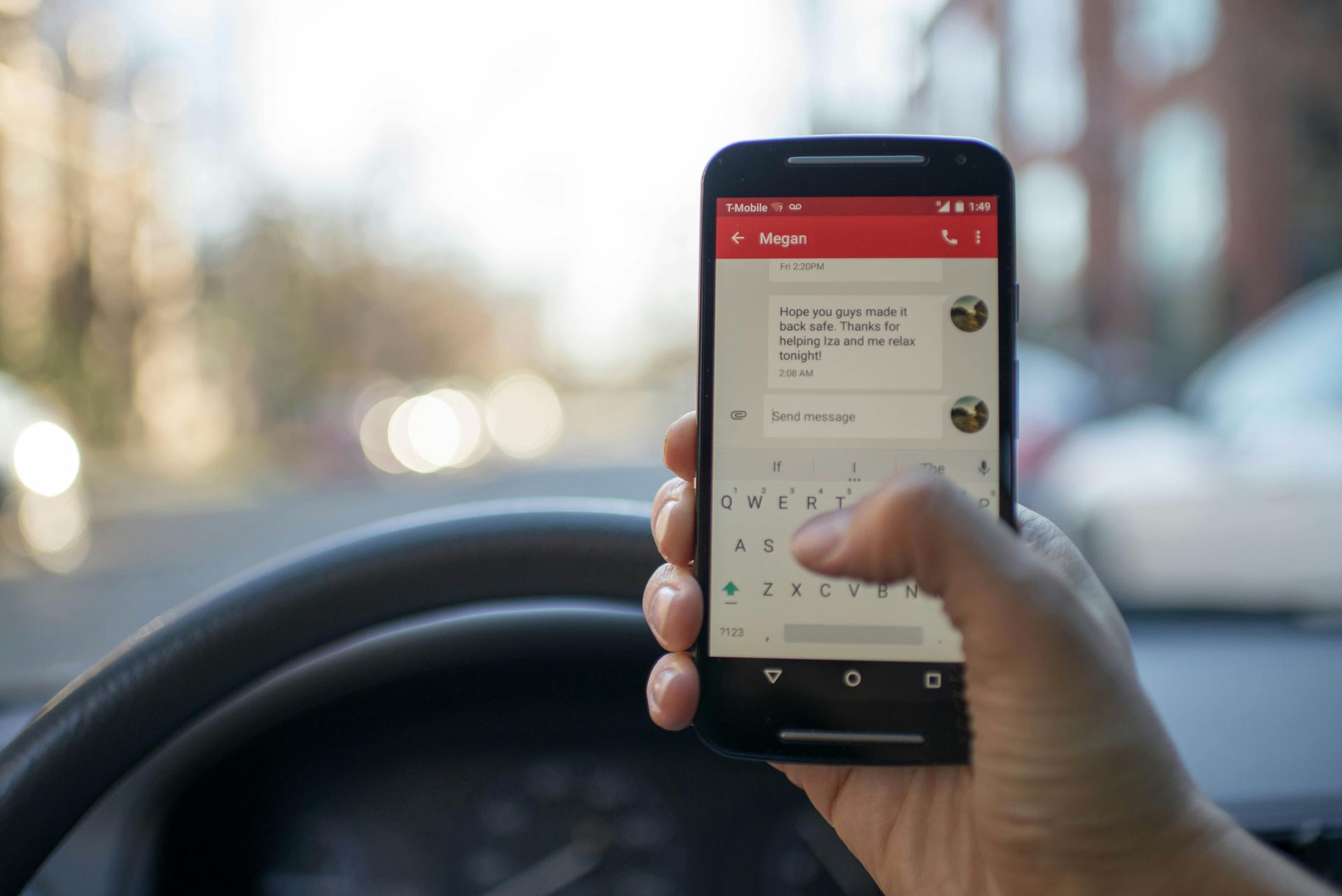 A person is holding a cell phone in their hand while driving a car.