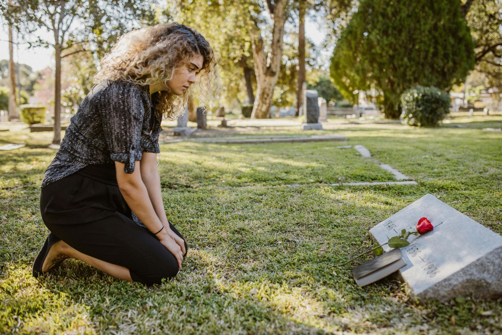 A woman is kneeling in front of a grave in a cemetery.