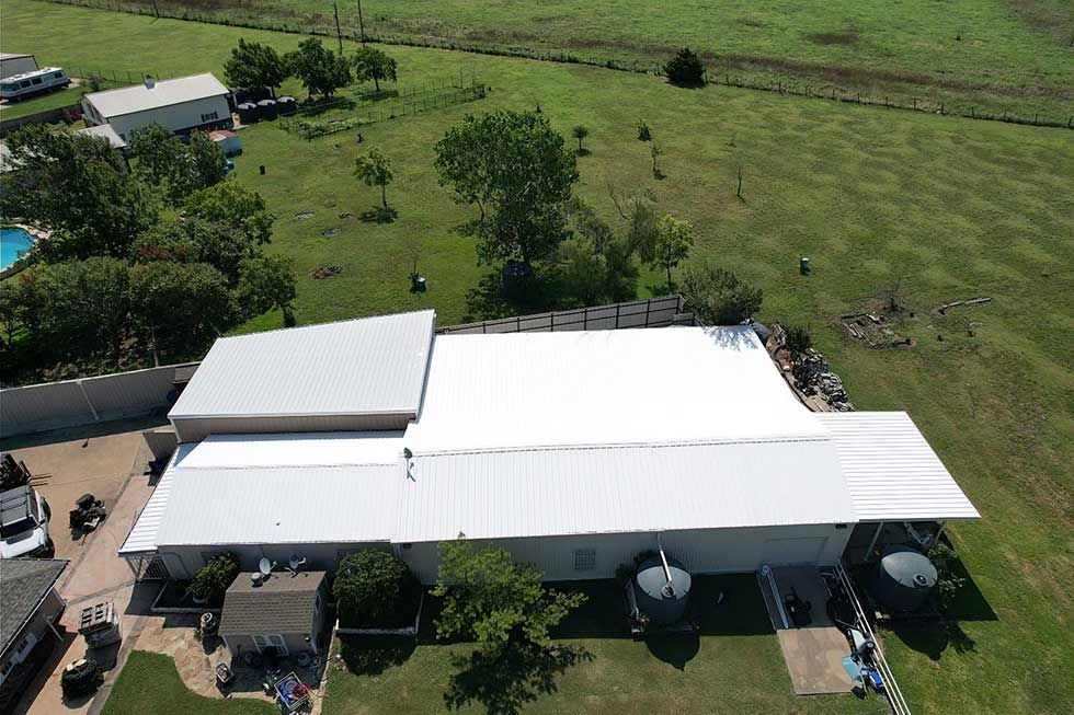 An aerial view of a house with a white roof surrounded by grass and trees.