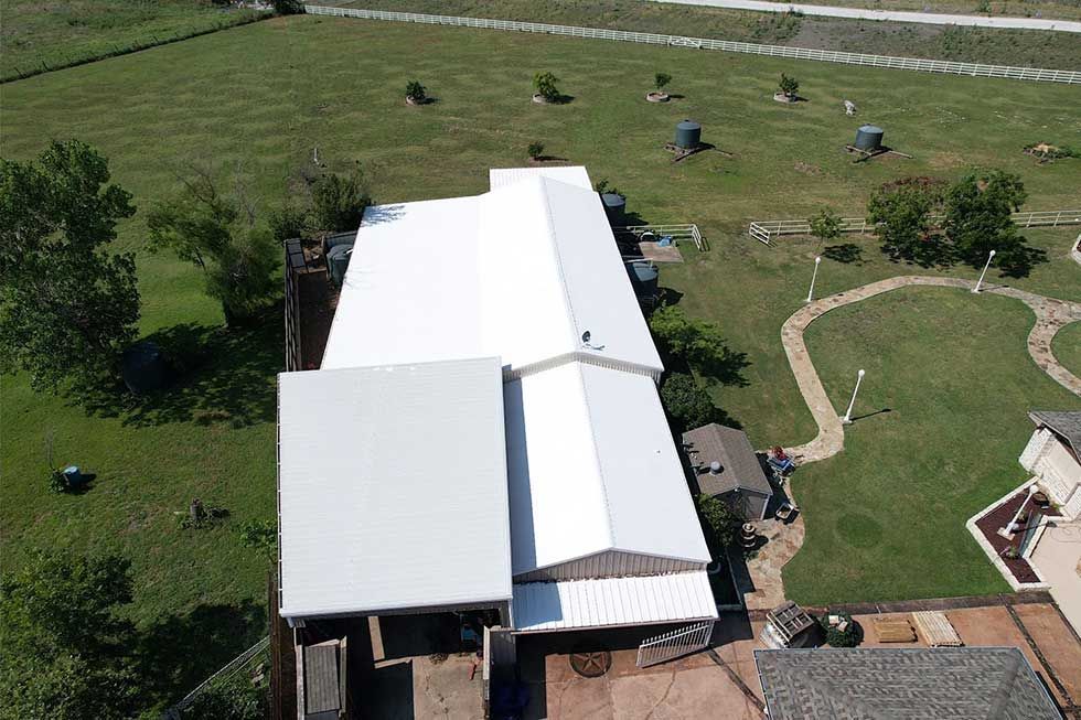 An aerial view of a house with a white roof surrounded by grass and trees.
