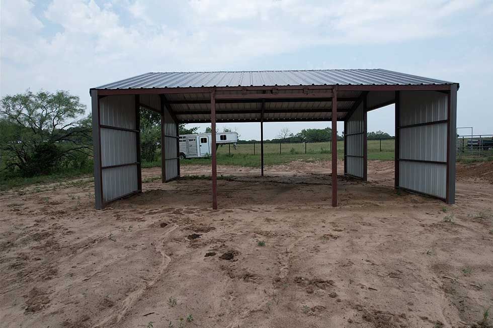 A metal building is sitting in the middle of a dirt field.