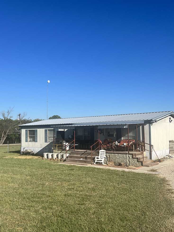 A mobile home with a porch and stairs is sitting on top of a lush green field.