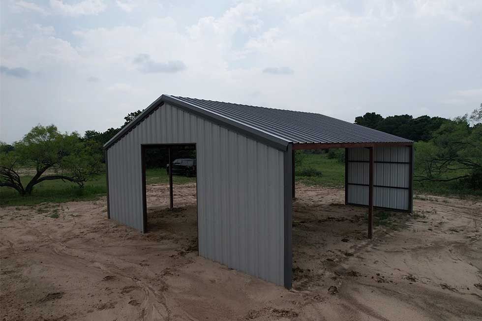 A metal barn is sitting in the middle of a dirt field.