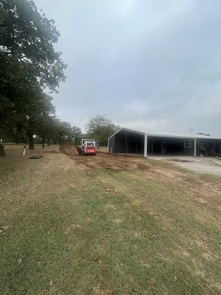 A bulldozer is driving down a dirt road in front of a building.
