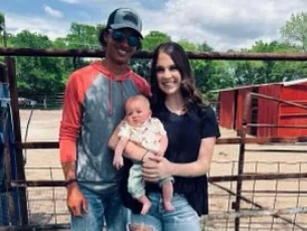 A man and a woman are holding a baby in front of a fence.